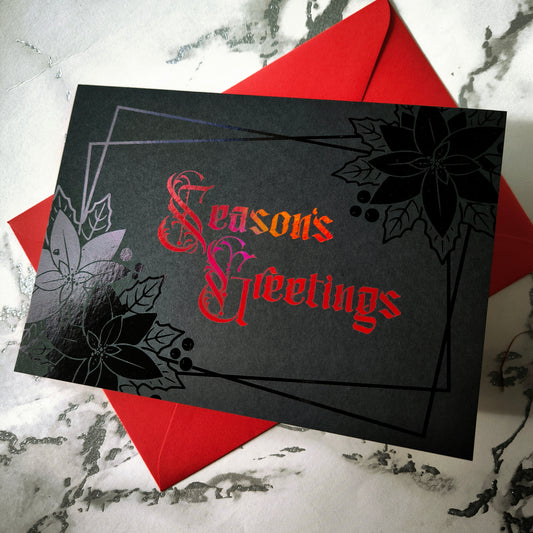 A5 landscape handmade Christmas card on black with red foil “Season’s Greetings” lettering and black foil poinsettia and holly motifs in the corners. Subtle border lines. Includes red envelope. Blank inside.