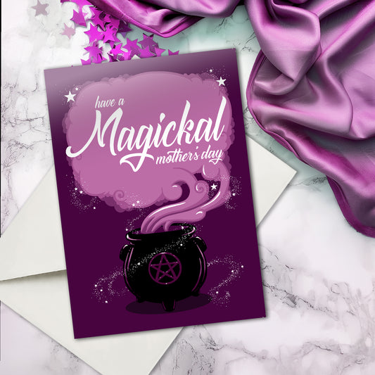 A large A5 greeting card in purple or pink, featuring a witchy cauldron illustration with billowing sparkling clouds and the words "Have a Magickal Mother’s Day." The inside has an illustration only (no text). Comes with an envelope included.