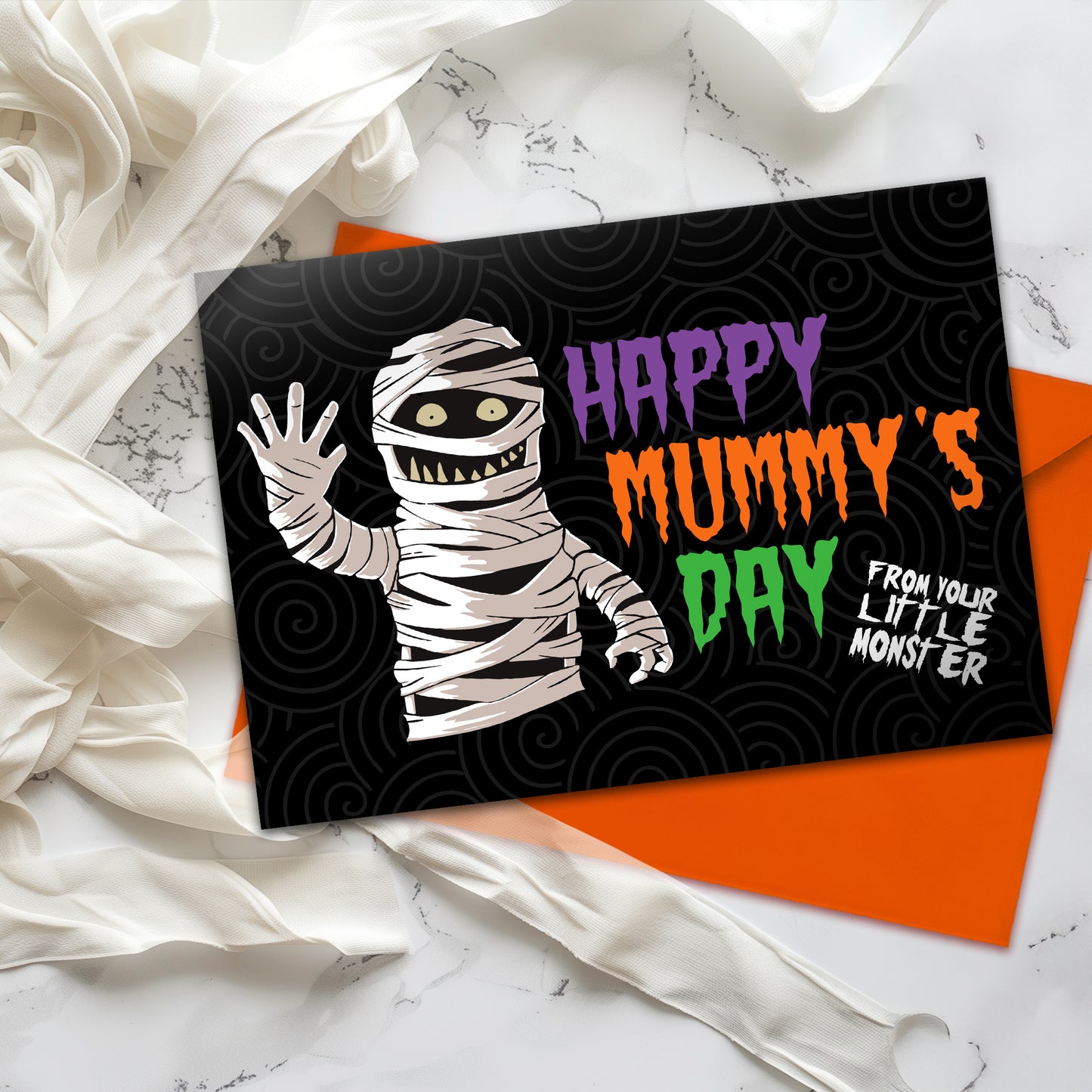 A large landscape A5 greeting card featuring a spooky cute mummy illustration with the phrase "Happy Mummy’s Day" in bold Halloween colours. The inside is decorated with a spiral motif but has no text. Comes with a bright orange envelope.