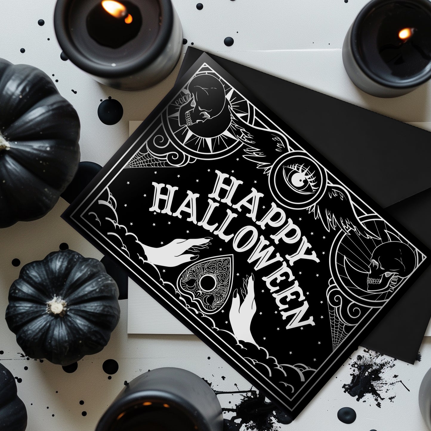 A black glossy A5 Halloween card with a white Ouija board-inspired “Happy Halloween” design, styled with gothic props on a dark background.