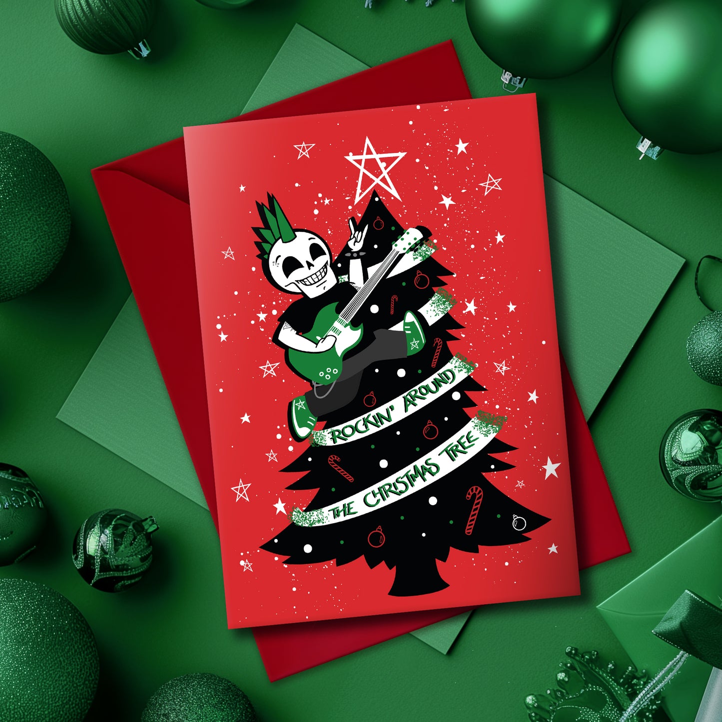 A5 glossy portrait Christmas card on red with black tree, white star and green ribbon reading “Rockin’ around the Christmas tree”. Skeleton with green mohawk plays electric guitar. Includes red envelope. Inside has small red star print with blank area.