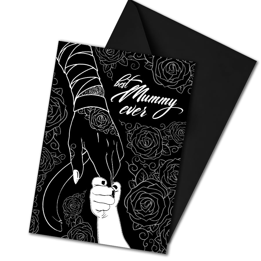 A large A5 glossy black greeting card featuring a tattoo-inspired illustration of a baby’s hand reaching for a woman’s hand wrapped in mummy bandages with rose tattoos. The card is framed by tattoo-style rose artwork. The inside is blank with matching rose motifs. Comes with an envelope included.