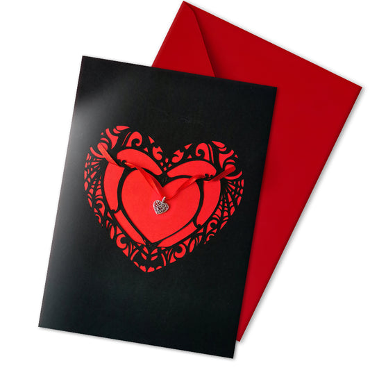 Handmade A5 black card with a red cut-out heart design and hanging silver heart charm on red ribbon. Blank white interior with envelope included. Perfect for gothic weddings, anniversaries, or alternative Valentine’s Day.