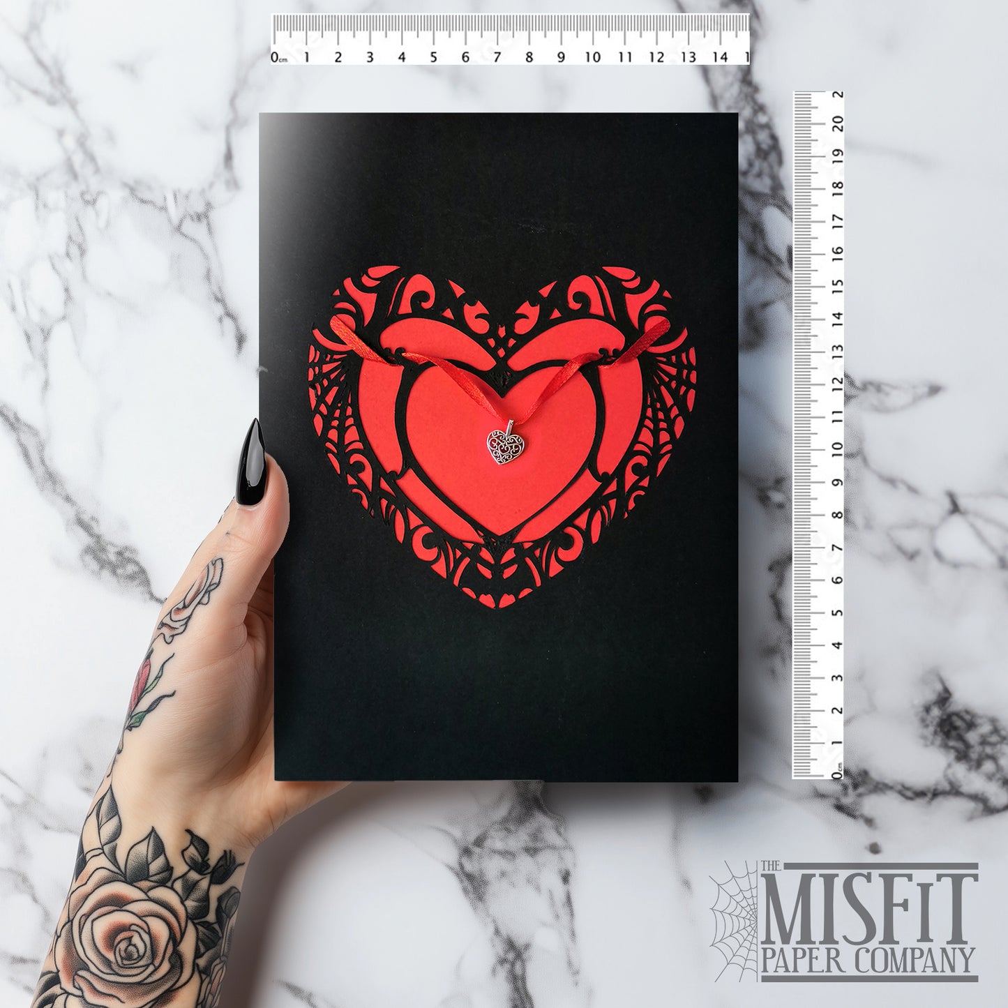 Handmade A5 black card with a red cut-out heart design and hanging silver heart charm on red ribbon. Blank white interior with envelope included. Perfect for gothic weddings, anniversaries, or alternative Valentine’s Day.