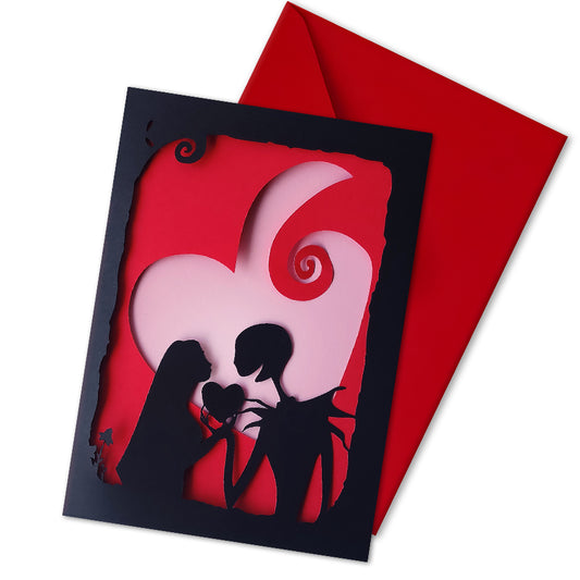 Handmade gothic romance card with black cut-out silhouette of Jack and Sally exchanging a heart, layered over a red heart with pink interior, A5 size.