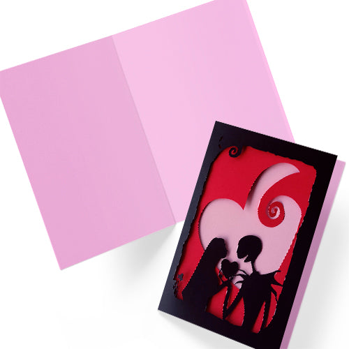 Handmade gothic romance card with black cut-out silhouette of Jack and Sally exchanging a heart, layered over a red heart with pink interior, A5 size.