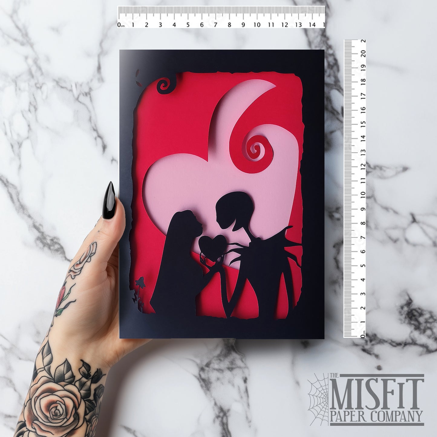 Handmade gothic romance card with black cut-out silhouette of Jack and Sally exchanging a heart, layered over a red heart with pink interior, A5 size.