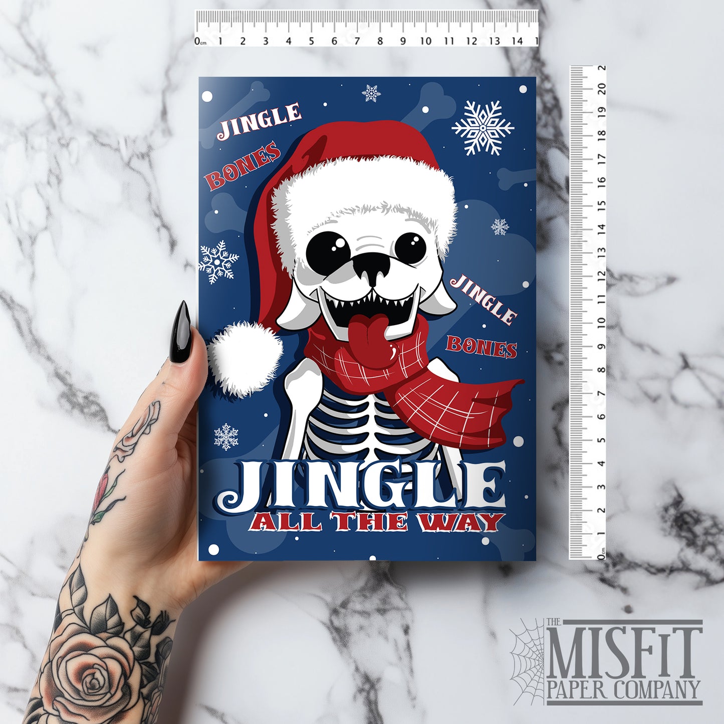 A5 glossy portrait Christmas card with cartoon skeleton dog wearing Santa hat and red scarf on dark blue background, snowflakes and “Jingle Bones” and "Jingle All The Way" text. Includes red envelope. Inside the lyric is completed with "Oh what fun it is to dig up treats in Santa's sleigh".