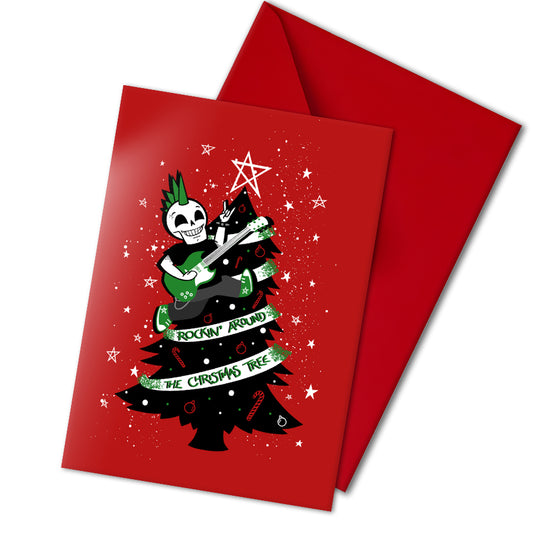 A5 glossy portrait Christmas card on red with black tree, white star and green ribbon reading “Rockin’ around the Christmas tree”. Skeleton with green mohawk plays electric guitar. Includes red envelope. Inside has small red star print with blank area.