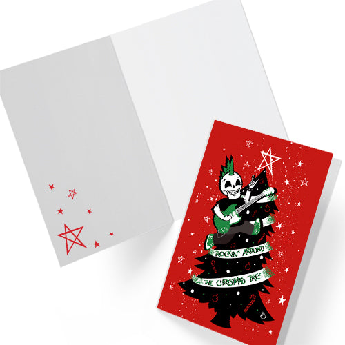 A5 glossy portrait Christmas card on red with black tree, white star and green ribbon reading “Rockin’ around the Christmas tree”. Skeleton with green mohawk plays electric guitar. Includes red envelope. Inside has small red star print with blank area.