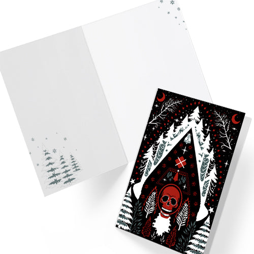 A5 glossy portrait greeting card with Scandi folk art design. Black background, white snowy pines, red crescents, stars, and a central red skull Santa motif. Graphic botanical details. Includes red envelope. Blank inside.