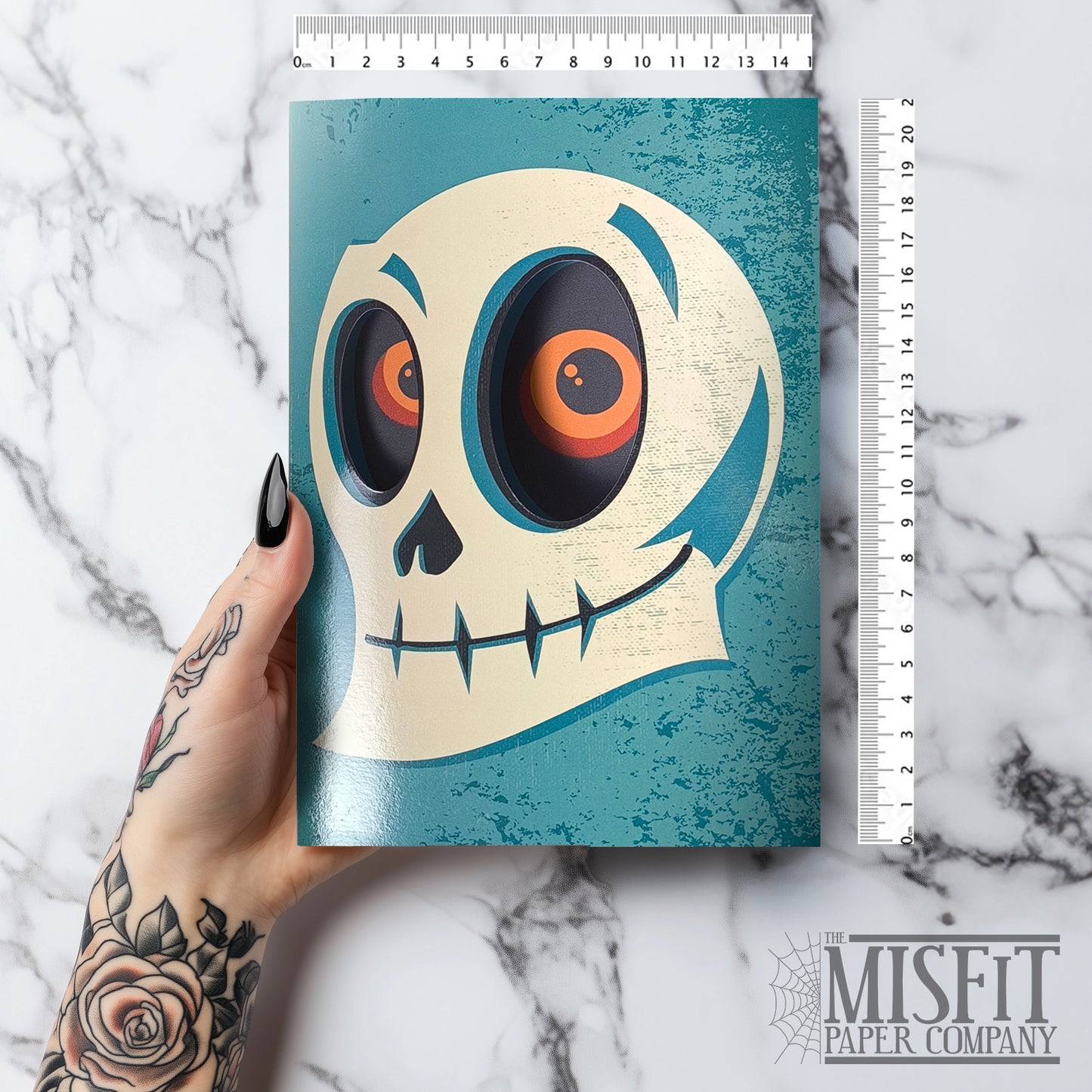 A glossy blue A5 Halloween card with a skull design, featuring cut-out eyes that reveal an eerie gaze inside, styled with gothic Halloween props.