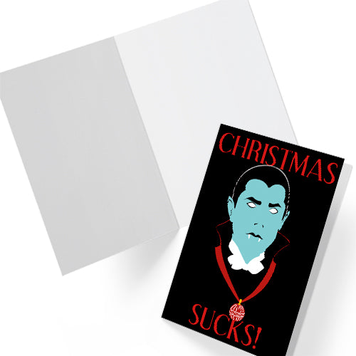 A5 glossy portrait greeting card with graphic vampire on black background, pale blue face, white eyes and fangs, red collar and bauble. Red serif text reads “CHRISTMAS SUCKS!”. Gothic, spooky style. Includes red envelope. Blank inside.