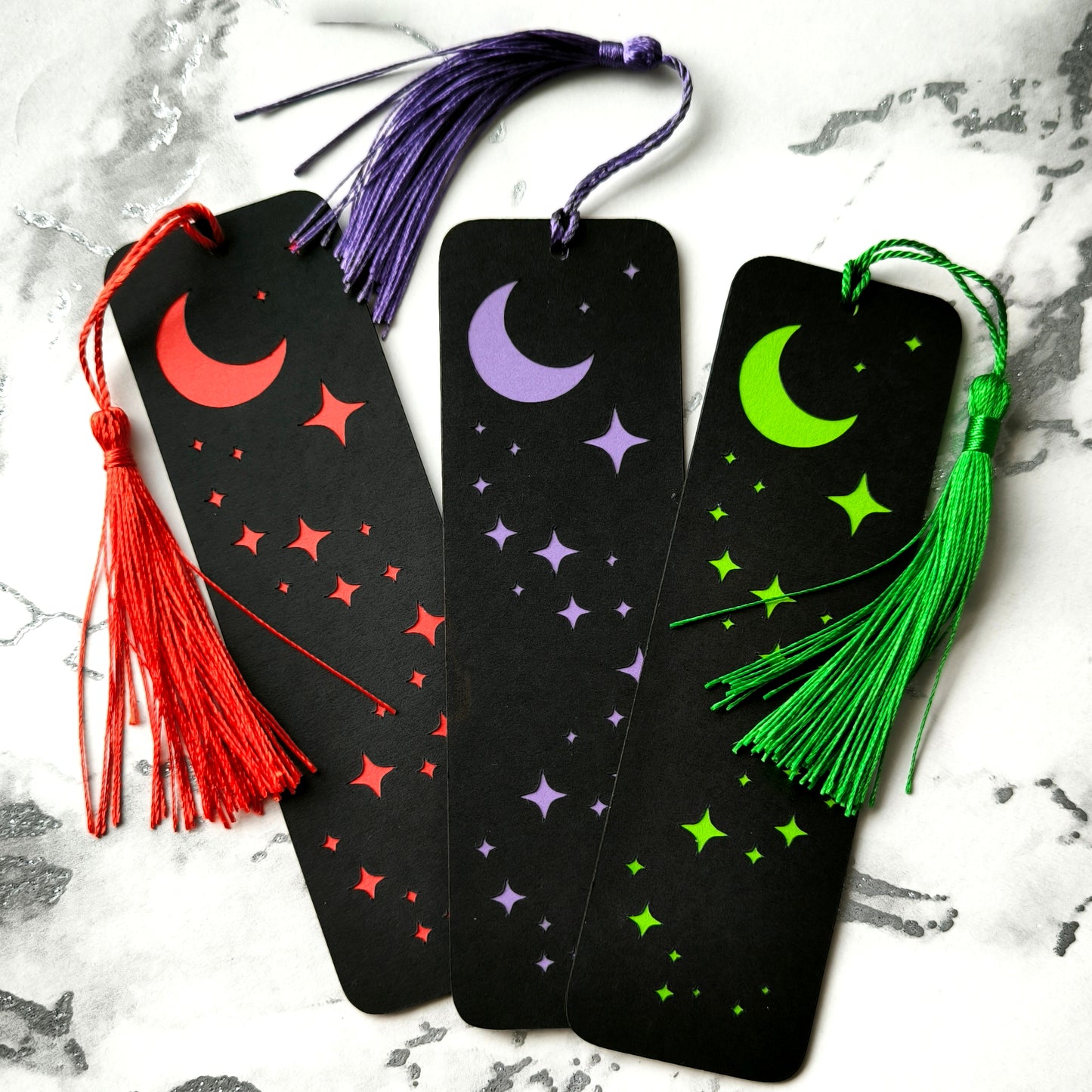 Custom gothic bookmarks with cutout names and celestial moon and star designs in red, purple, green, gold, and silver, with matching tassels