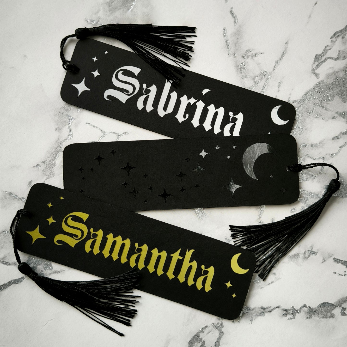 Custom gothic bookmarks with cutout names and celestial moon and star designs in red, purple, green, gold, and silver, with matching tassels