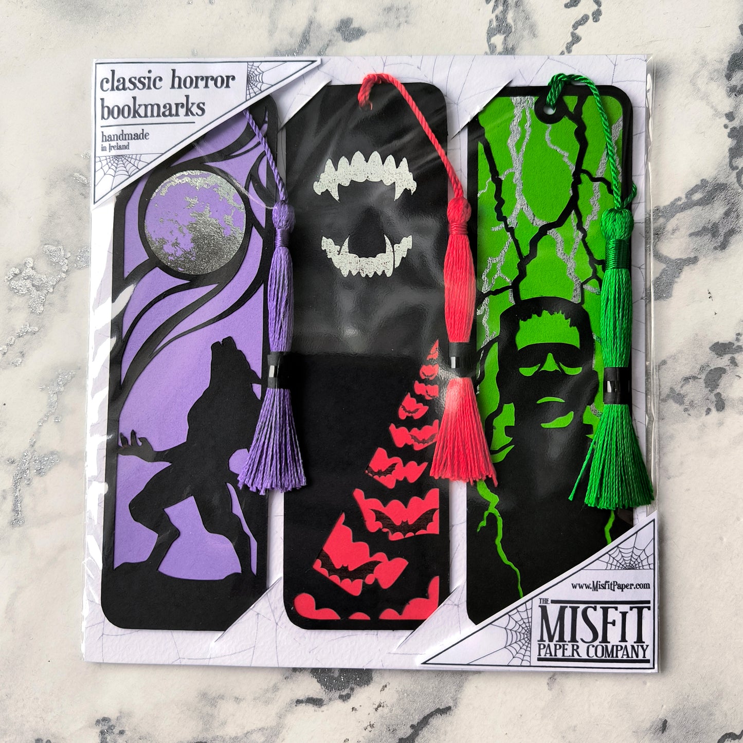 Set of 3 gothic bookmarks featuring classic horror icons: a howling werewolf, Dracula fangs, and Frankenstein’s monster. Each with dark backgrounds, metallic details, bold designs, and matching tassels. Perfect for horror fans and alternative book lovers.