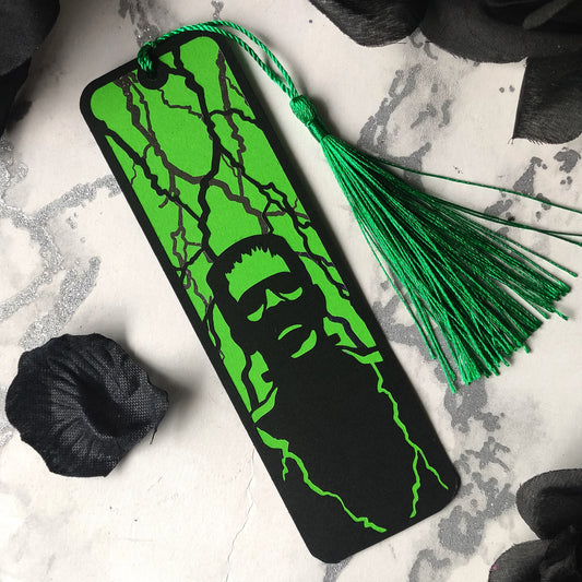 Gothic black bookmark featuring the silhouette of frankenstein's monster over a green background and silver metallic lightning strikes. Finished with a matching tassel. Perfect for horror and classic literature fans.