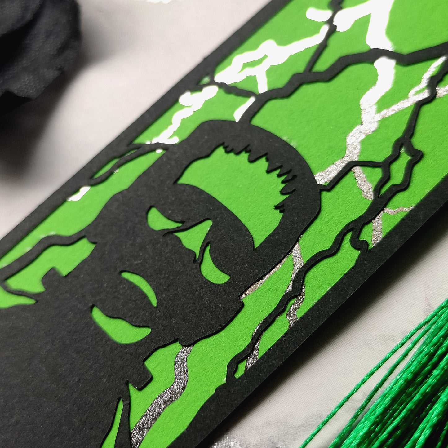 Gothic black bookmark featuring the silhouette of frankenstein's monster over a green background and silver metallic lightning strikes. Finished with a matching tassel. Perfect for horror and classic literature fans.