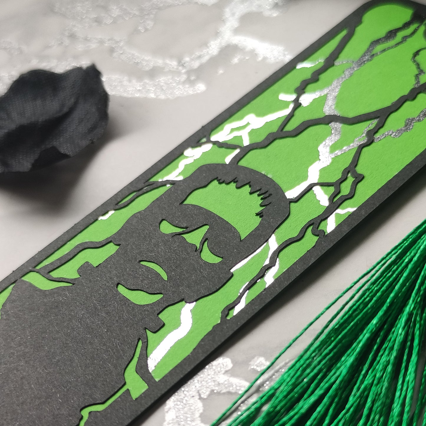 Gothic black bookmark featuring the silhouette of frankenstein's monster over a green background and silver metallic lightning strikes. Finished with a matching tassel. Perfect for horror and classic literature fans.