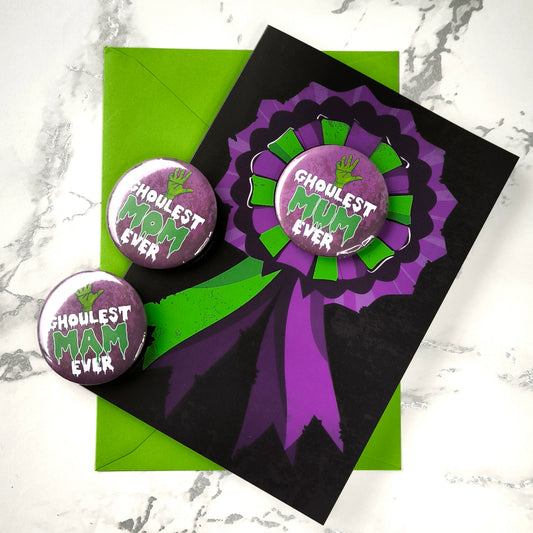 A large glossy A5 greeting card featuring a green and purple rosette with a removable 58mm badge reading "Ghoulest Mom Ever" in a bold, spooky font. Available in Mom, Mum, or Mam variations. The card is blank inside and comes with an envelope.