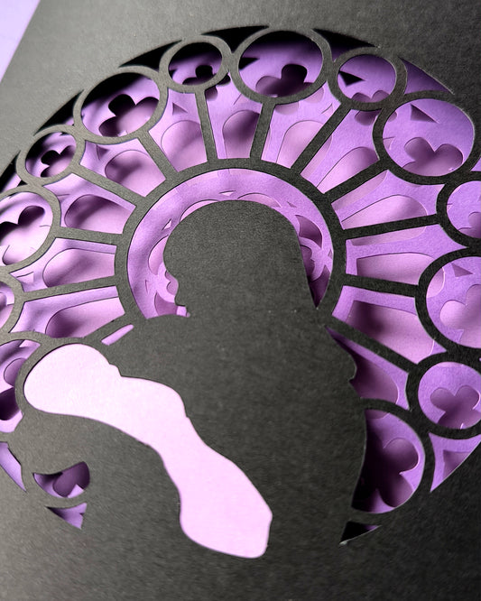 Handmade papercut greeting card, with a layered rose window in purple and black. Features a mother and baby silhouette in front of the gothic cathedral window design. Includes matching purple envelope.