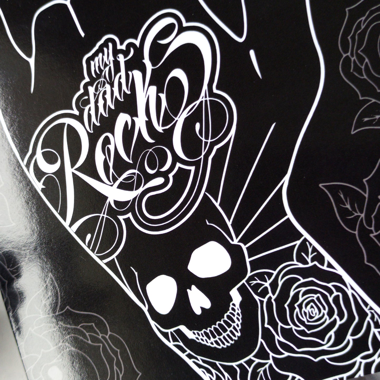 Glossy black Father’s Day card featuring a hand throwing the rock horns with skull and rose tattoos, and the phrase “My Dad Rocks” in ink lettering.