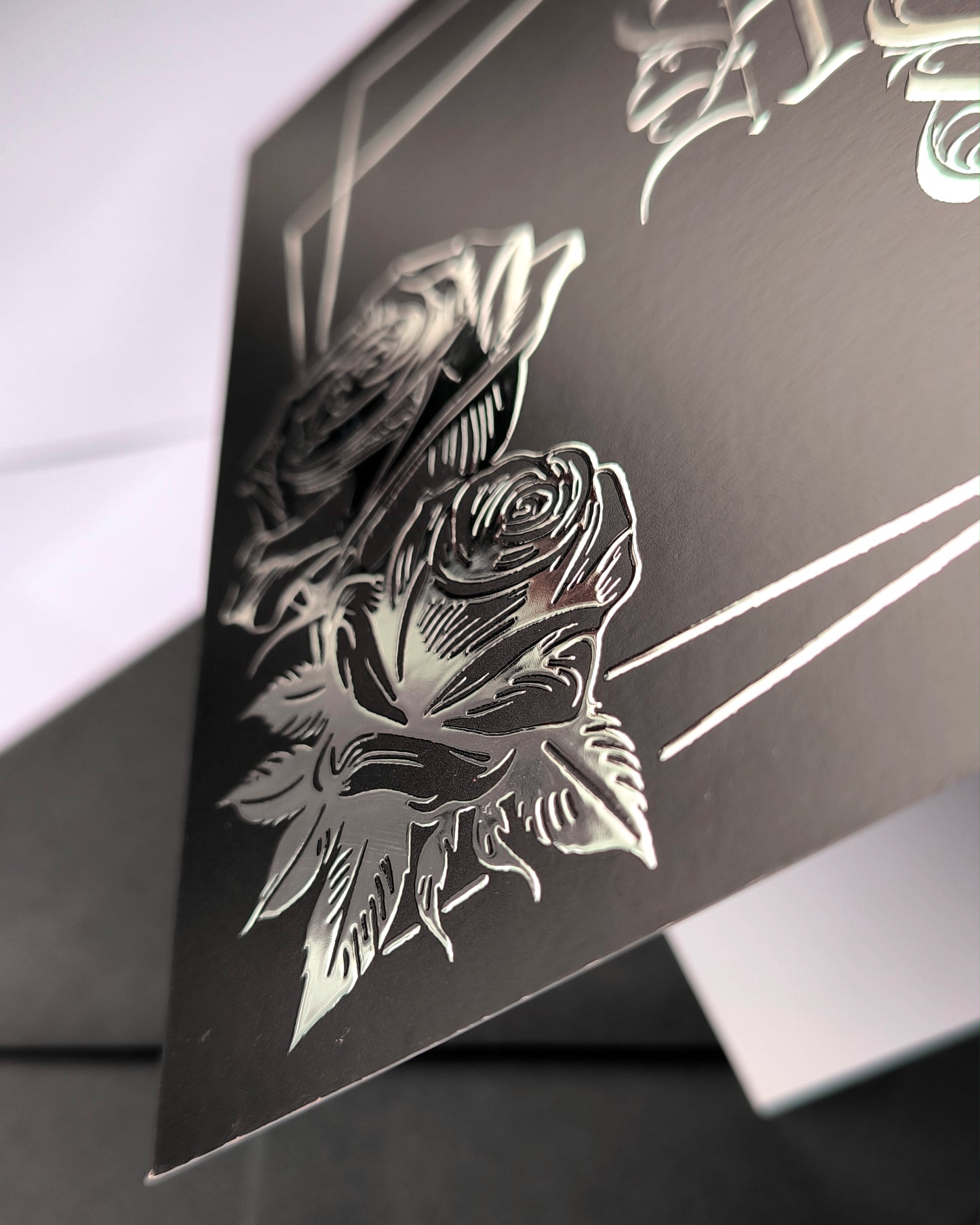 A smooth black card with raised silver chrome detailing. Silver gothic text reads Happy Birthday, surrounded by a silver rectangular frame and silver roses in two corners.