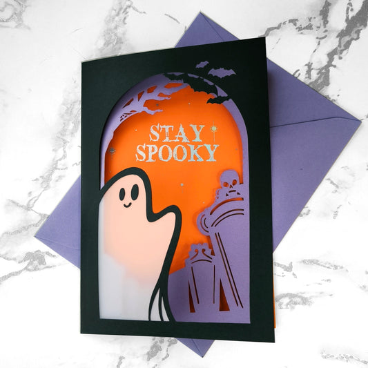Handmade Halloween ghost greeting card with layered black, orange, and purple paper. Features a translucent ghost, holographic "Stay Spooky" lettering, and gothic graveyard scene.