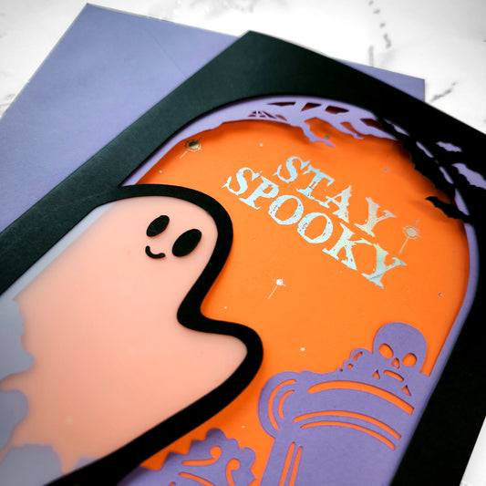 Handmade Halloween ghost greeting card with layered black, orange, and purple paper. Features a translucent ghost, holographic "Stay Spooky" lettering, and gothic graveyard scene.
