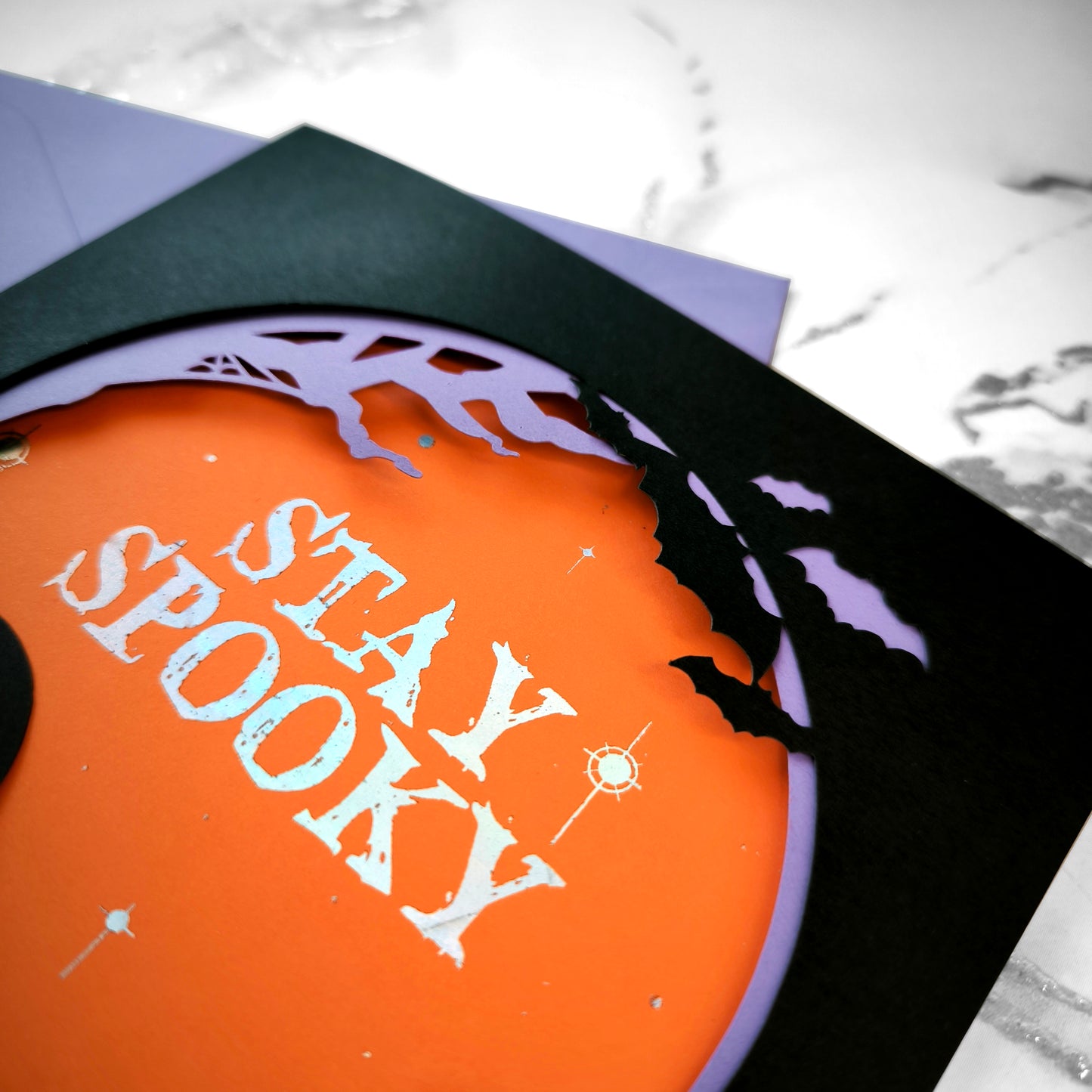 Handmade Halloween ghost greeting card with layered black, orange, and purple paper. Features a translucent ghost, holographic "Stay Spooky" lettering, and gothic graveyard scene.
