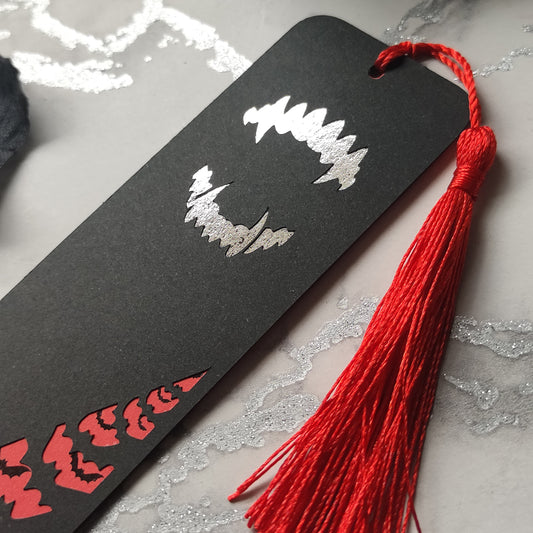 Gothic Dracula bookmark with silver metallic fangs and a flock of black foil bats flying across a deep red background. Finished with a matching tassel. Perfect for fans of vampires, classic horror, and dark, alternative literature.