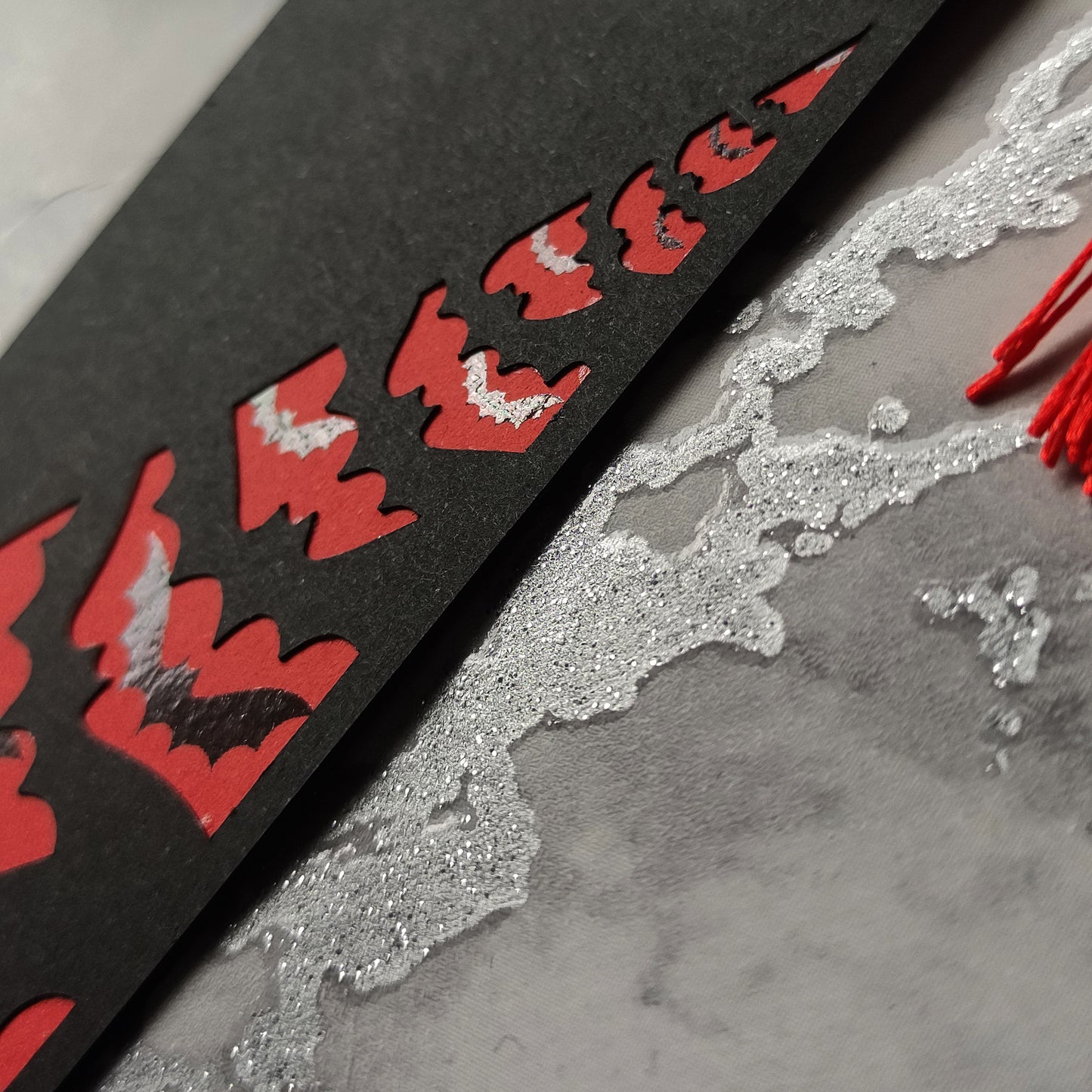 Gothic Dracula bookmark with silver metallic fangs and a flock of black foil bats flying across a deep red background. Finished with a matching tassel. Perfect for fans of vampires, classic horror, and dark, alternative literature.