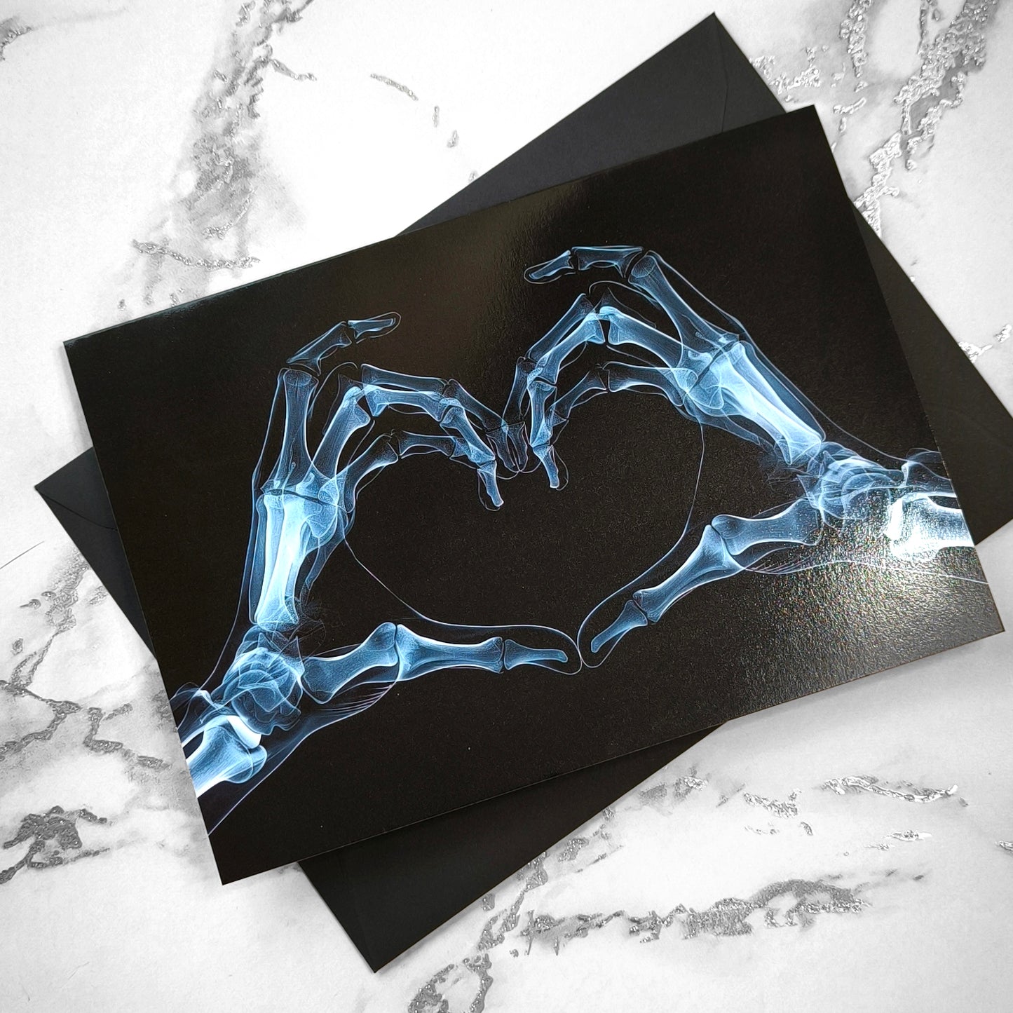 Large A5 gothic greeting card with a skeleton X-ray image of two hands forming a heart on a glossy black background. Blank inside, with envelope included. Ideal for alternative Valentine’s Day, anniversaries, or dark romance gestures.