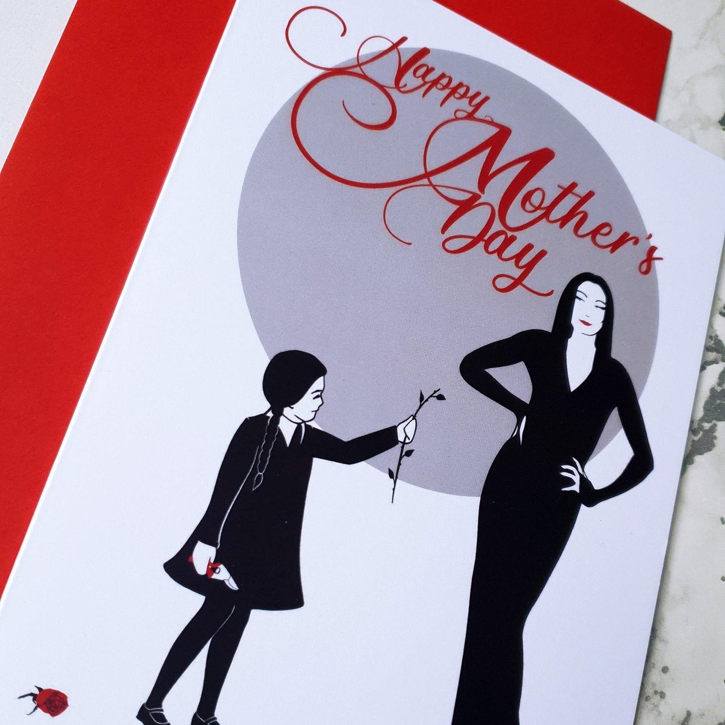 Large A5 glossy Mother’s Day card featuring Wednesday Addams giving Morticia a headless rose, with Pugsley causing mischief on the back. Includes red envelope and blank interior, perfect for spooky, gothic, and alternative mums.