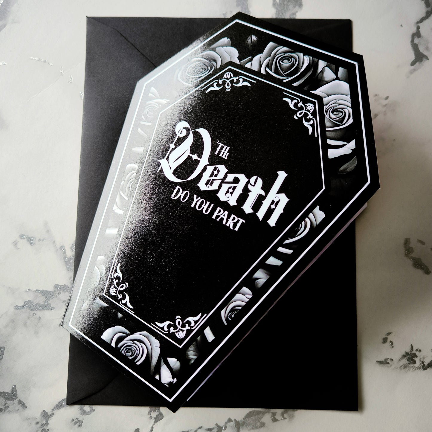 Coffin-shaped gothic wedding or anniversary card with the phrase "Til Death Do You Part" or "Til Death Do Us Part" on a black background, surrounded by monochrome roses. Subtle black and white rose inner print and a black envelope.
