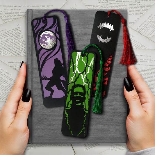 Set of 3 gothic bookmarks featuring classic horror icons: a howling werewolf, Dracula fangs, and Frankenstein’s monster. Each with dark backgrounds, metallic details, bold designs, and matching tassels. Perfect for horror fans and alternative book lovers.