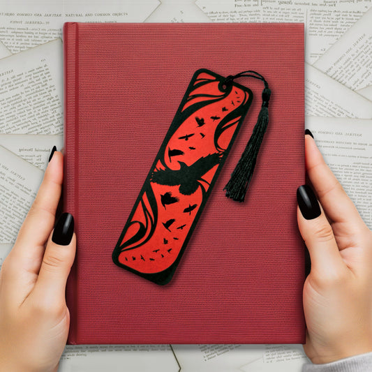 A handmade card bookmark. the black top layer is cut to a sweeping crow silhouette framed by flowing lines, set against a blood-red base scattered with glossy black-foiled crows in flight. Finished with a sleek black tassel.