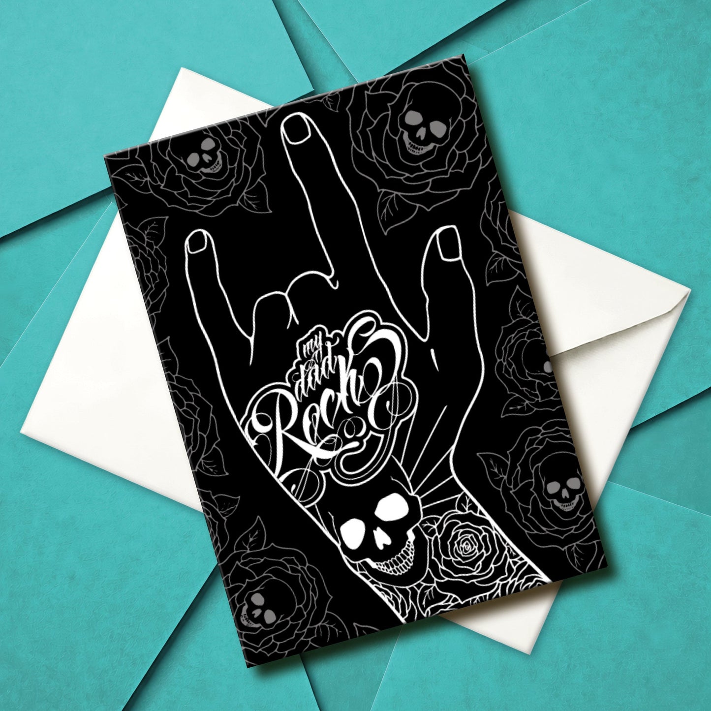 Glossy black Father’s Day card featuring a hand throwing the rock horns with skull and rose tattoos, and the phrase “My Dad Rocks” in ink lettering.