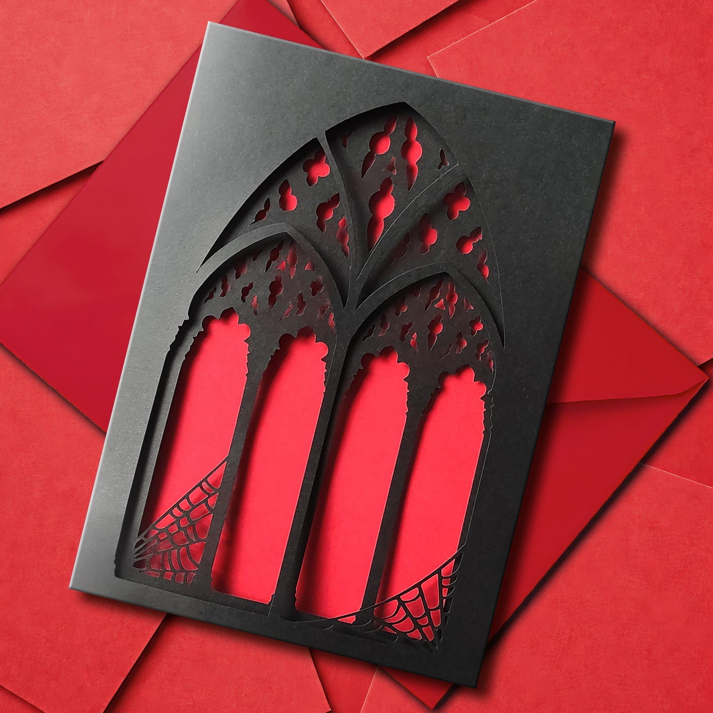 A handmade black greeting card with two intricate papercut layers of a gothic cathedral window with spiderwebs in the corners. Your choice of blood red or lilac purple shows between the window arches. Comes with a matching colour envelope.