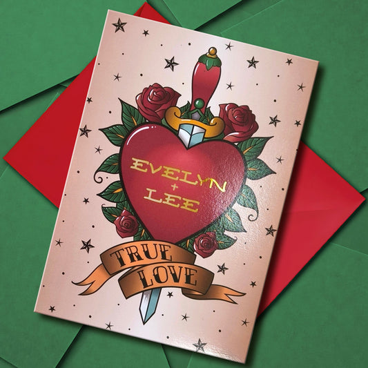 A personalised couples greeting card inspired by traditional tattoo designs. A red heart with an ornate handled dagger vertically through it, is surrounded by roses and stars. Underneath it, a banner reads "true love" in traditional tattoo text. the custom gold foiled text inside the heart reads the couple's names. Inside another similar banner reads "forever". Perfect for wedding guests, anniversary or valentines.