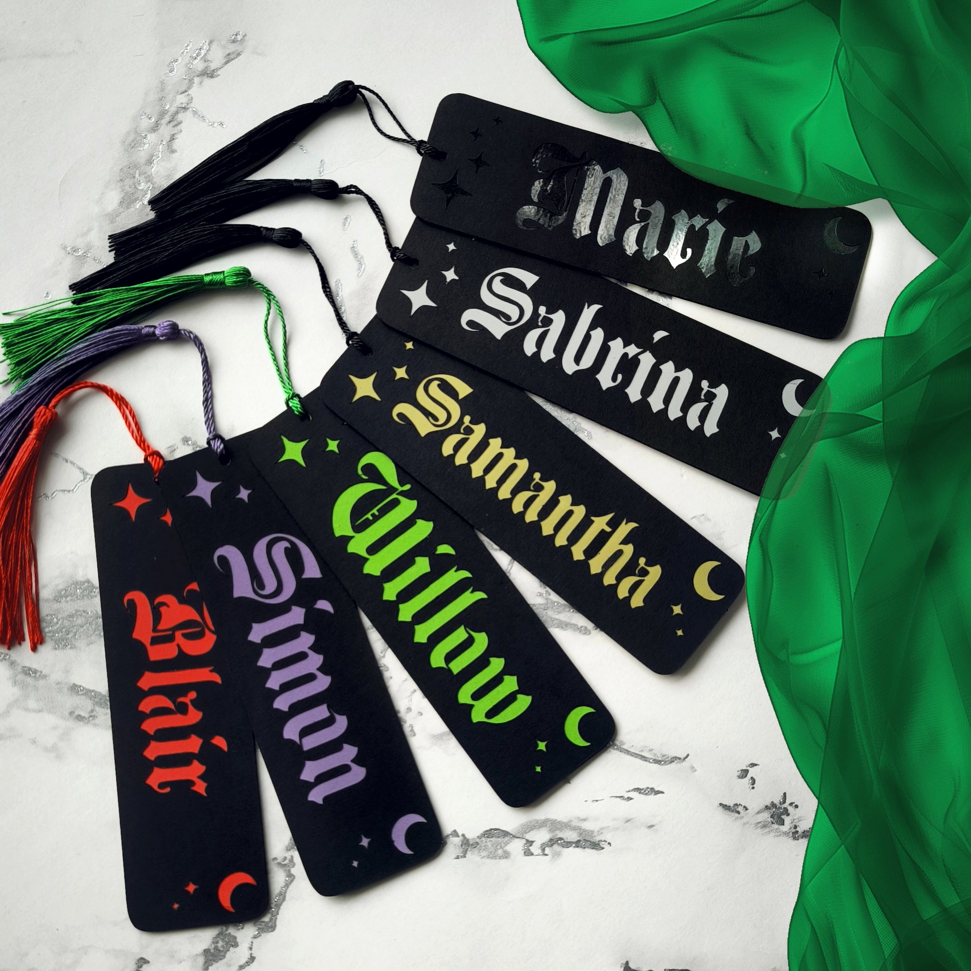 Custom gothic bookmarks with cutout names and celestial moon and star designs in red, purple, green, gold, and silver, with matching tassels