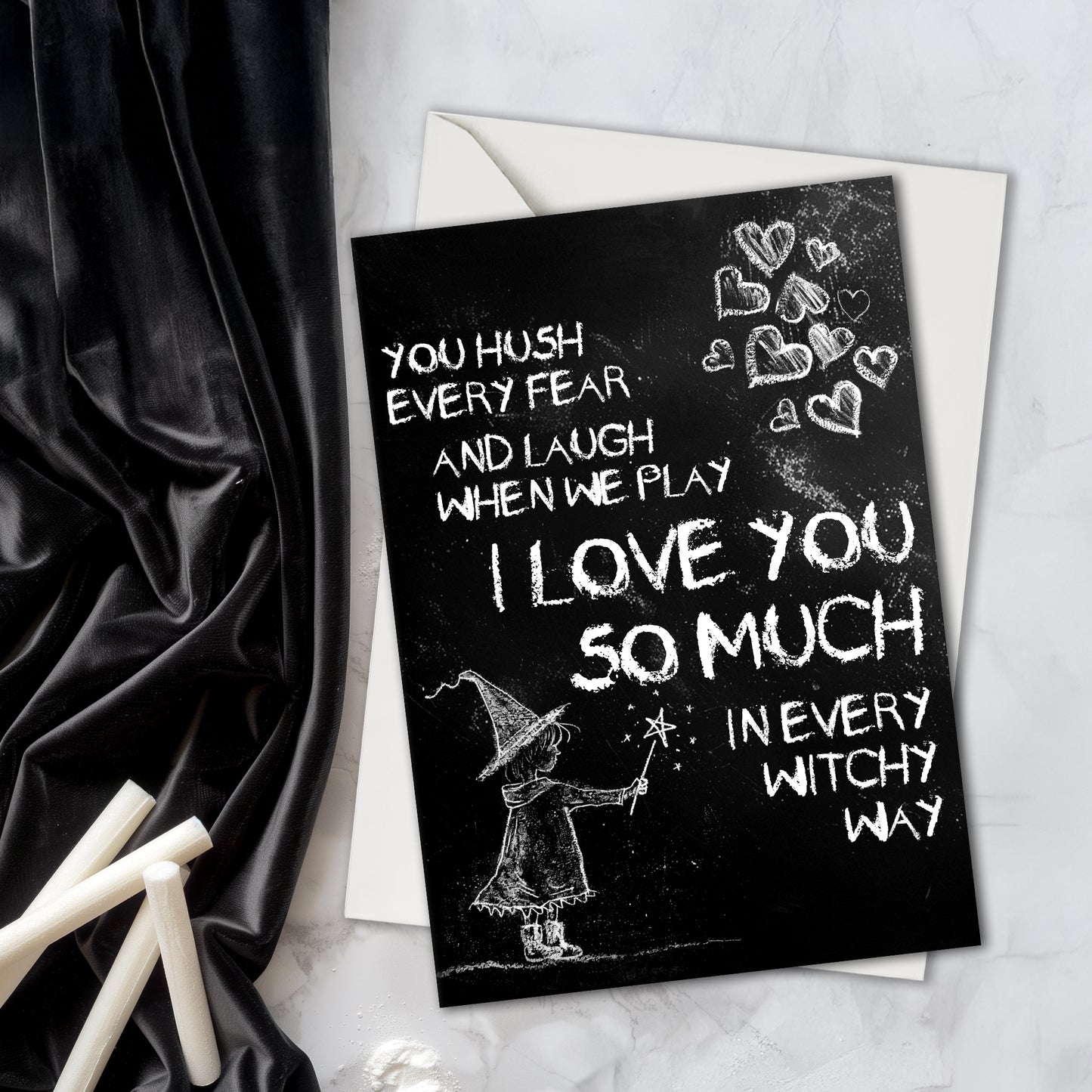 A black A5 greeting card with a chalkboard-style background, featuring a hand-drawn witch illustration casting a spell with floating love hearts. A sweet rhyming poem is written in chalk-style lettering. The card reads Happy Mother's Day inside and comes with an envelope.