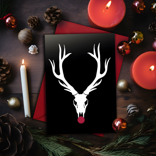 A5 glossy portrait Christmas card with white reindeer skull and large antlers on black background, bright red circle for Rudolph's nose. Minimal graphic style. Includes red envelope. Blank inside.