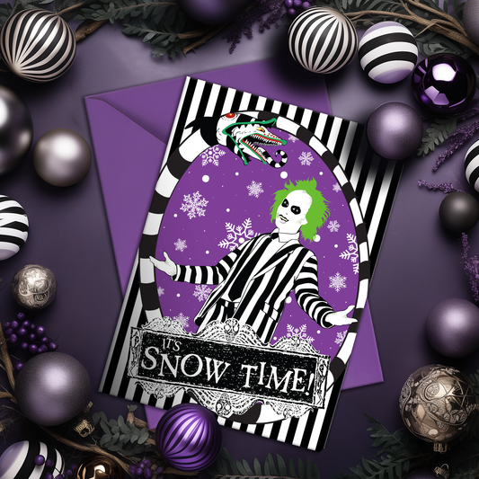A5 glossy portrait Christmas card with black and white striped frame, purple background and snowflakes. Green-haired Beetlejuice in pinstripe suit, sandworm at top, banner reads “It’s Snow Time!”. Includes purple envelope. Blank inside.