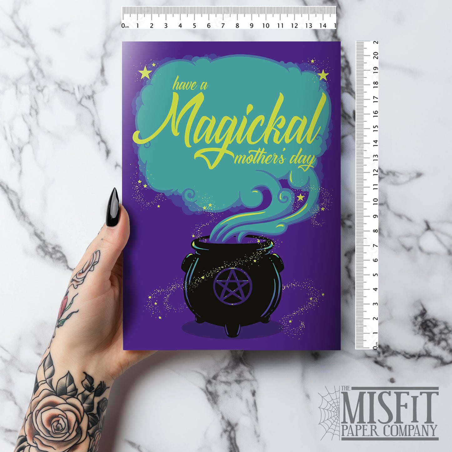 A large A5 greeting card in purple or pink, featuring a witchy cauldron illustration with billowing sparkling clouds and the words "Have a Magickal Mother’s Day." The inside has an illustration only (no text). Comes with an envelope included.