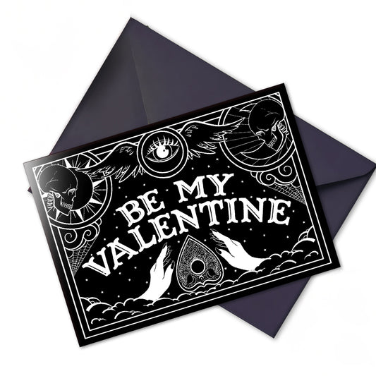 A black and white card with a ouija board design, and the text "Be My Valentine" in a gothic font. The card features an intricate spooky design and an interior illustration.