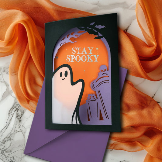 Handmade Halloween ghost greeting card with layered black, orange, and purple paper. Features a translucent ghost, holographic "Stay Spooky" lettering, and gothic graveyard scene.