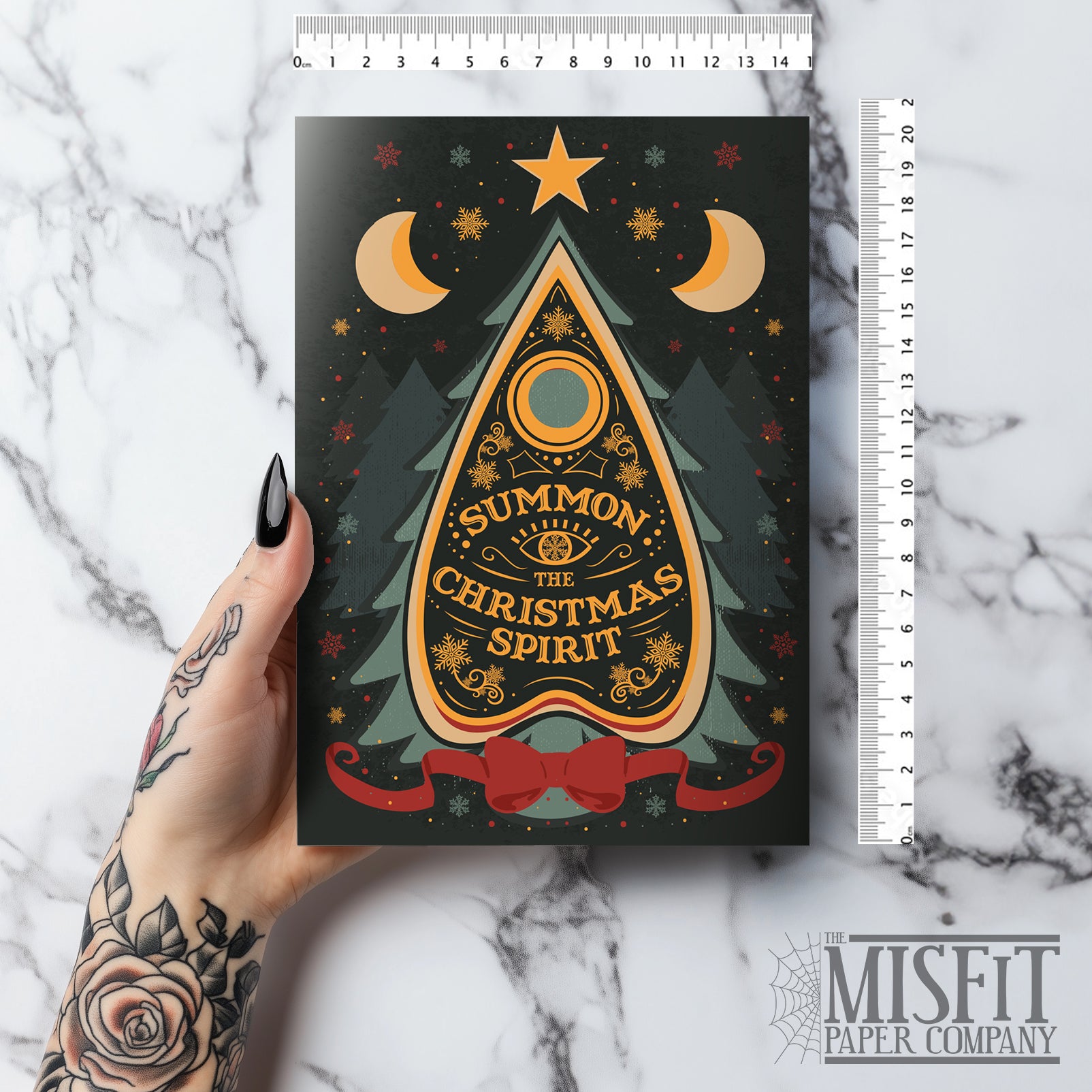 A5 glossy portrait Christmas card on black with ornate Ouija planchette reading “Summon the Christmas Spirit”, moons, stars, snowflakes and pine tree shapes with gold and green details. Cream envelope. Inside has pale green border with snowflake corners, blank area.
