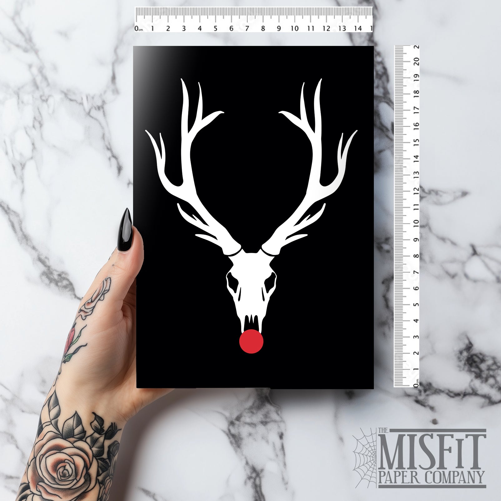 A5 glossy portrait Christmas card with white reindeer skull and large antlers on black background, bright red circle for Rudolph's nose. Minimal graphic style. Includes red envelope. Blank inside.