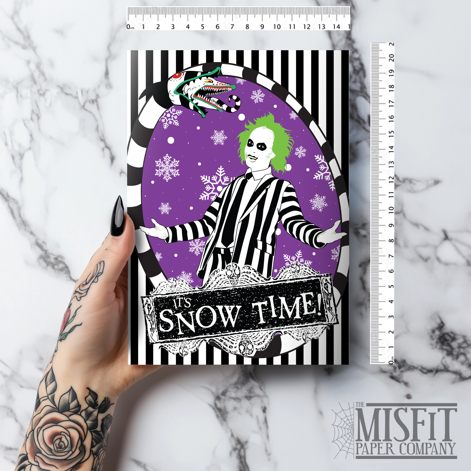 A5 glossy portrait Christmas card with black and white striped frame, purple background and snowflakes. Green-haired Beetlejuice in pinstripe suit, sandworm at top, banner reads “It’s Snow Time!”. Includes purple envelope. Blank inside.
